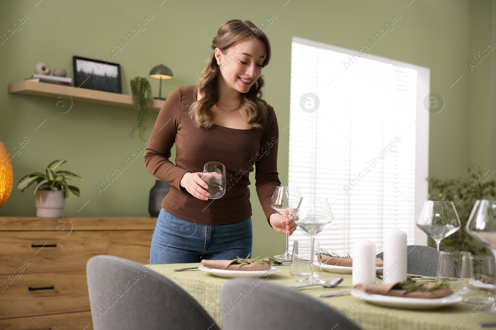 Photo of Happy young woman setting table for dinner at home