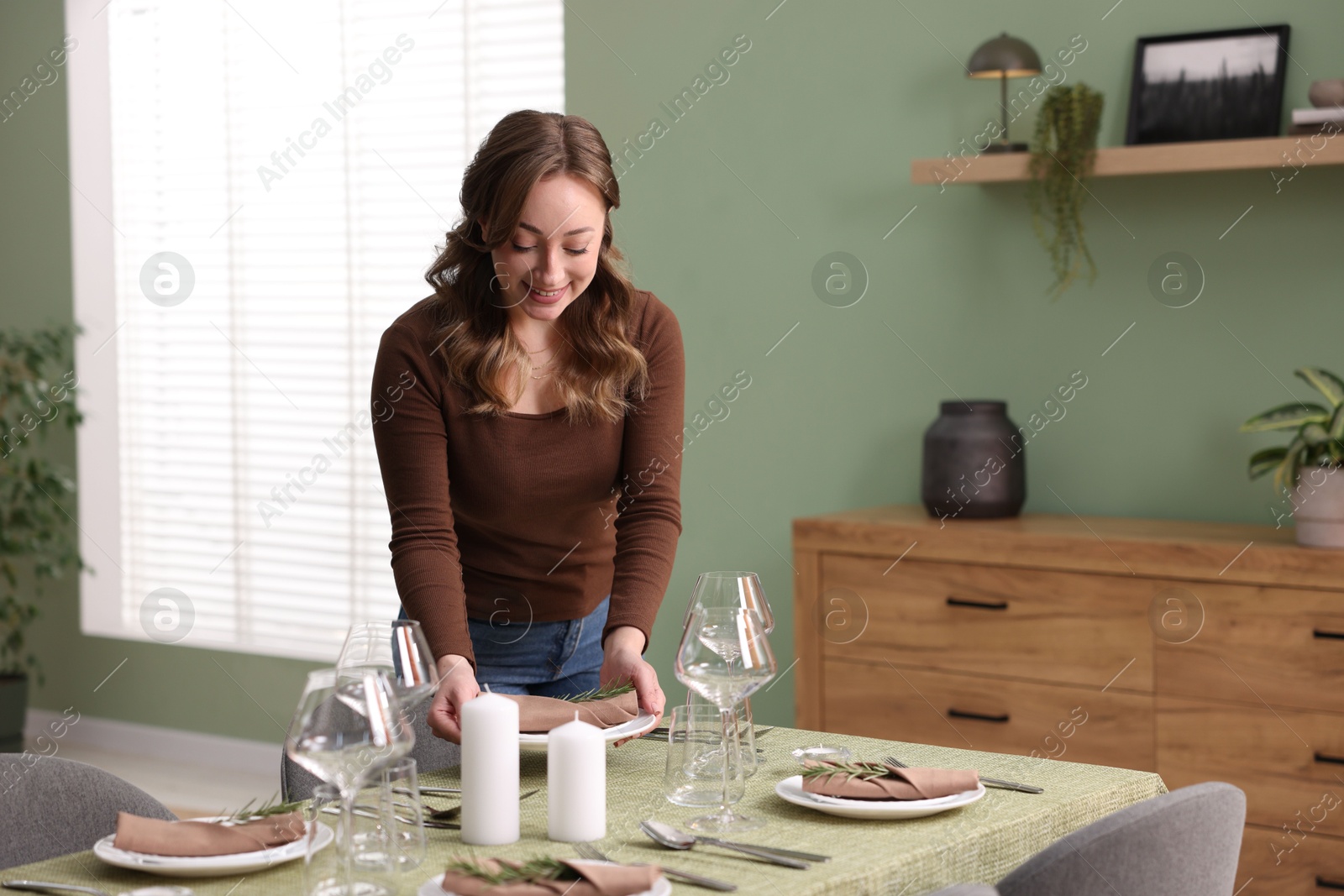 Photo of Happy young woman setting table for dinner at home