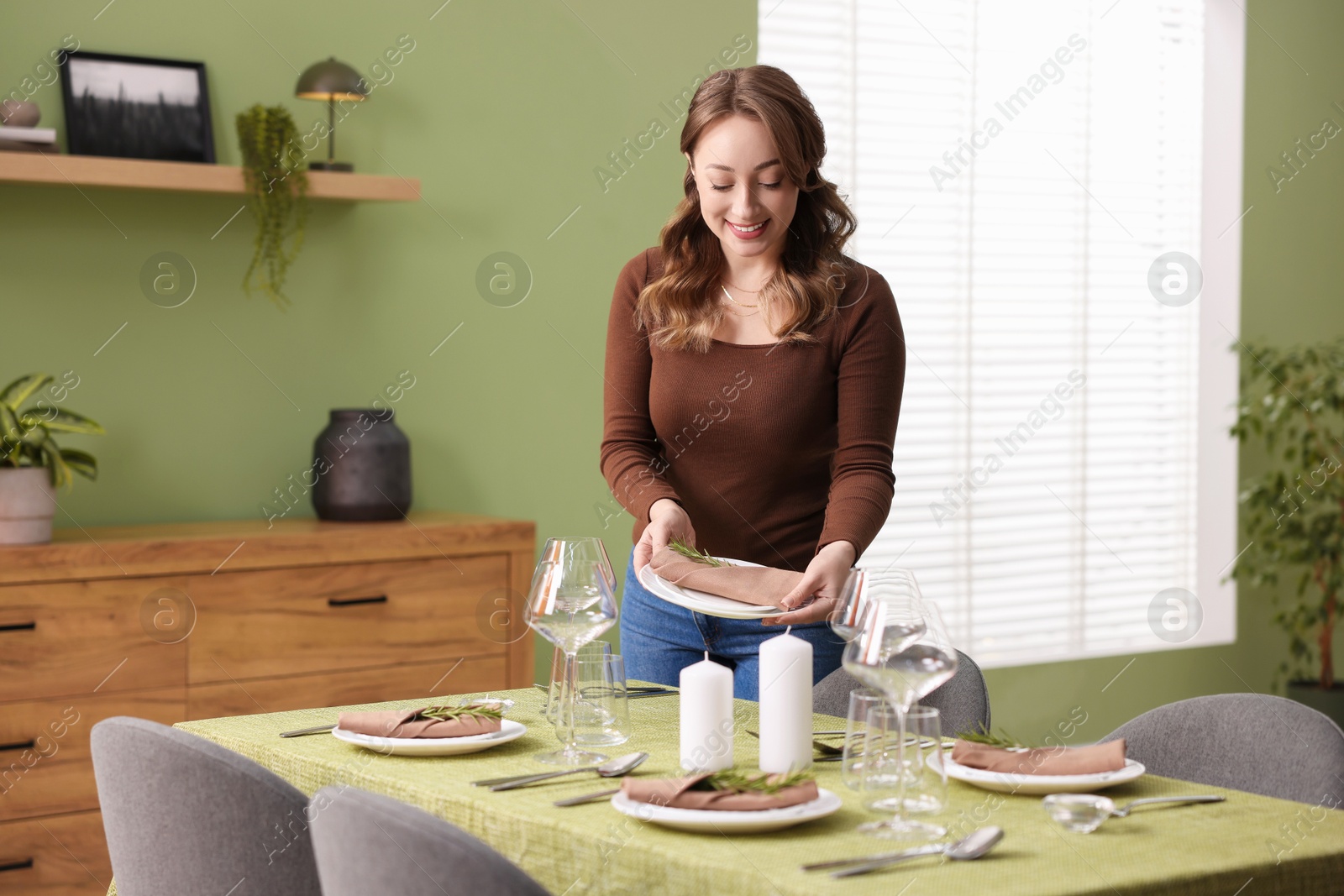 Photo of Happy young woman setting table for dinner at home