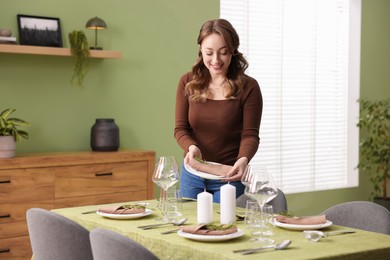 Happy young woman setting table for dinner at home