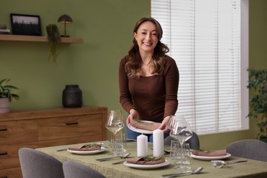 Happy young woman setting table for dinner at home