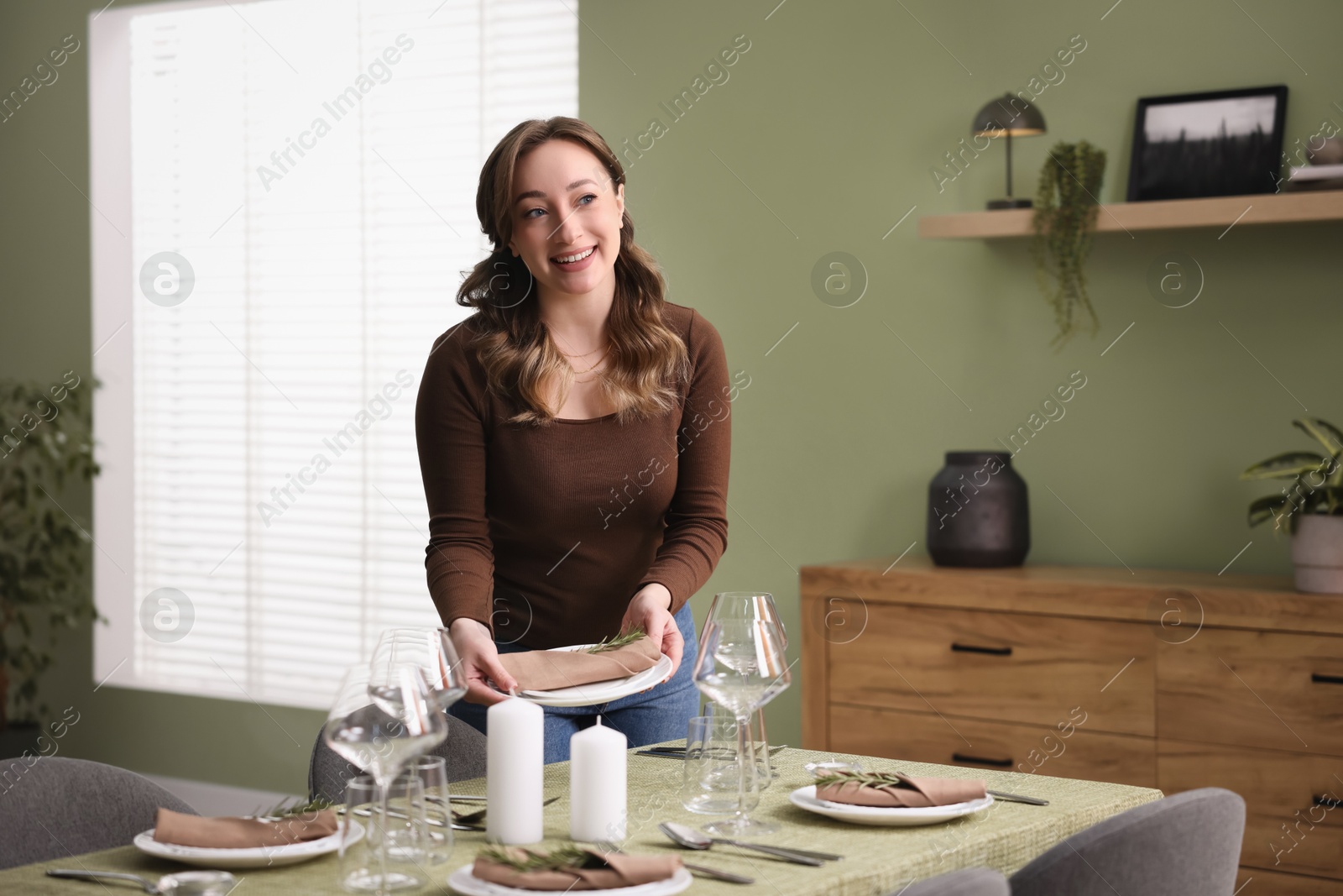 Photo of Happy young woman setting table for dinner at home