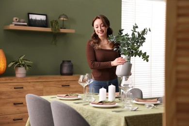 Happy young woman setting table for dinner at home