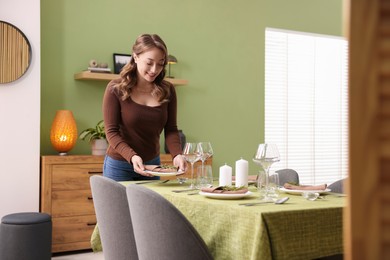 Photo of Happy young woman setting table for dinner at home