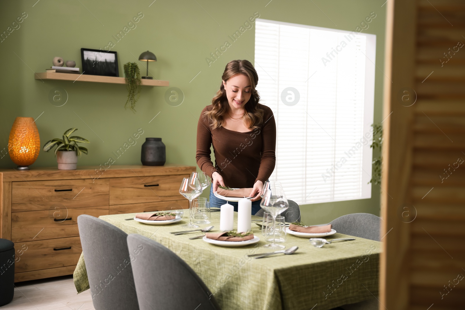 Photo of Happy young woman setting table for dinner at home