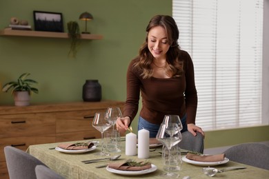 Happy young woman setting table for dinner at home