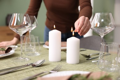 Woman lighting candles at table indoors, closeup