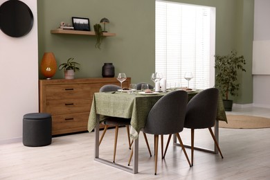 Photo of Stylish table setting with olive tablecloth, glasses and candles in dining room