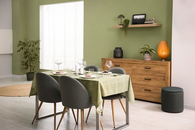 Photo of Stylish table setting with olive tablecloth, glasses and candles in dining room