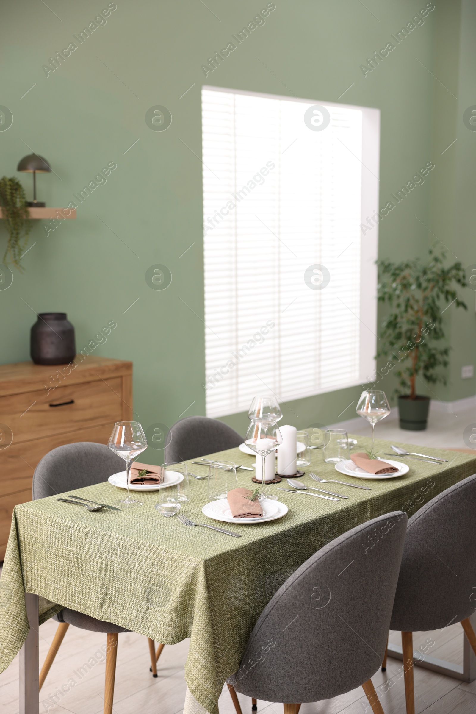 Photo of Stylish table setting with olive tablecloth, glasses and candles in dining room