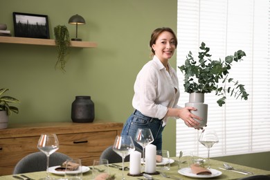 Happy young woman setting table for dinner at home