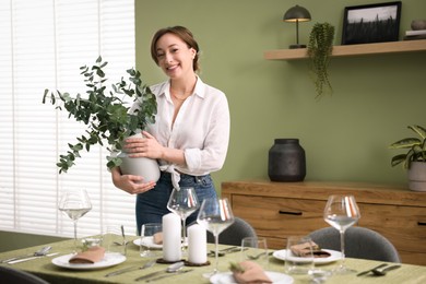 Happy young woman setting table for dinner at home