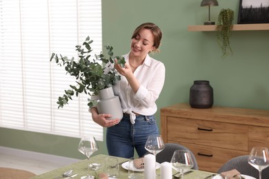 Happy young woman setting table for dinner at home