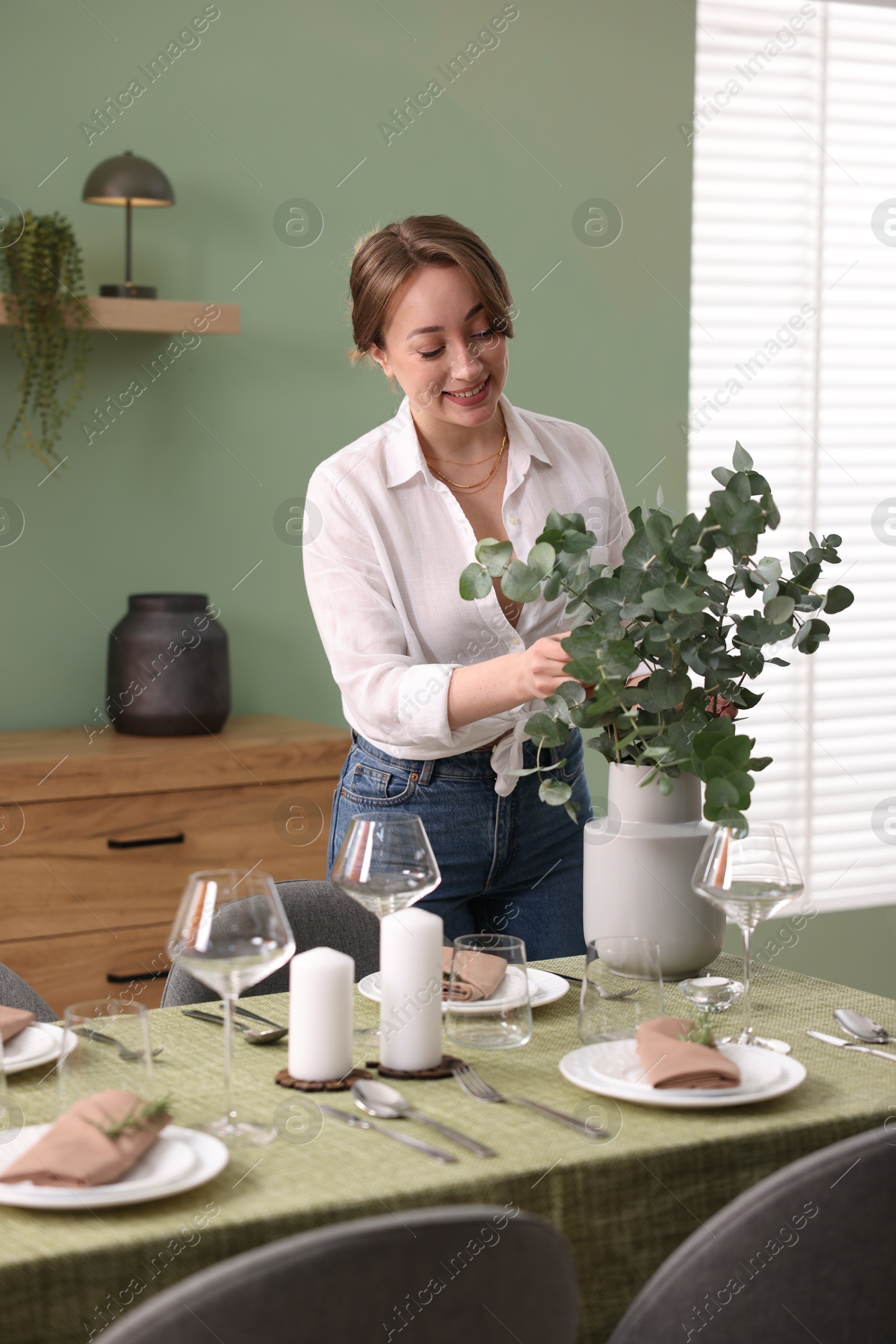 Photo of Happy young woman setting table for dinner at home