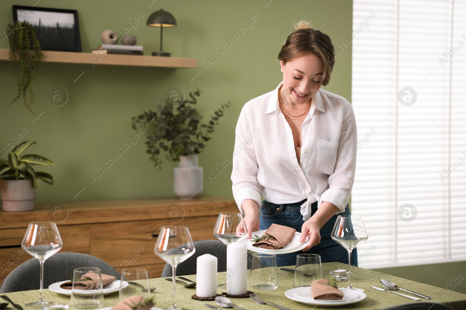 Photo of Happy young woman setting table for dinner at home