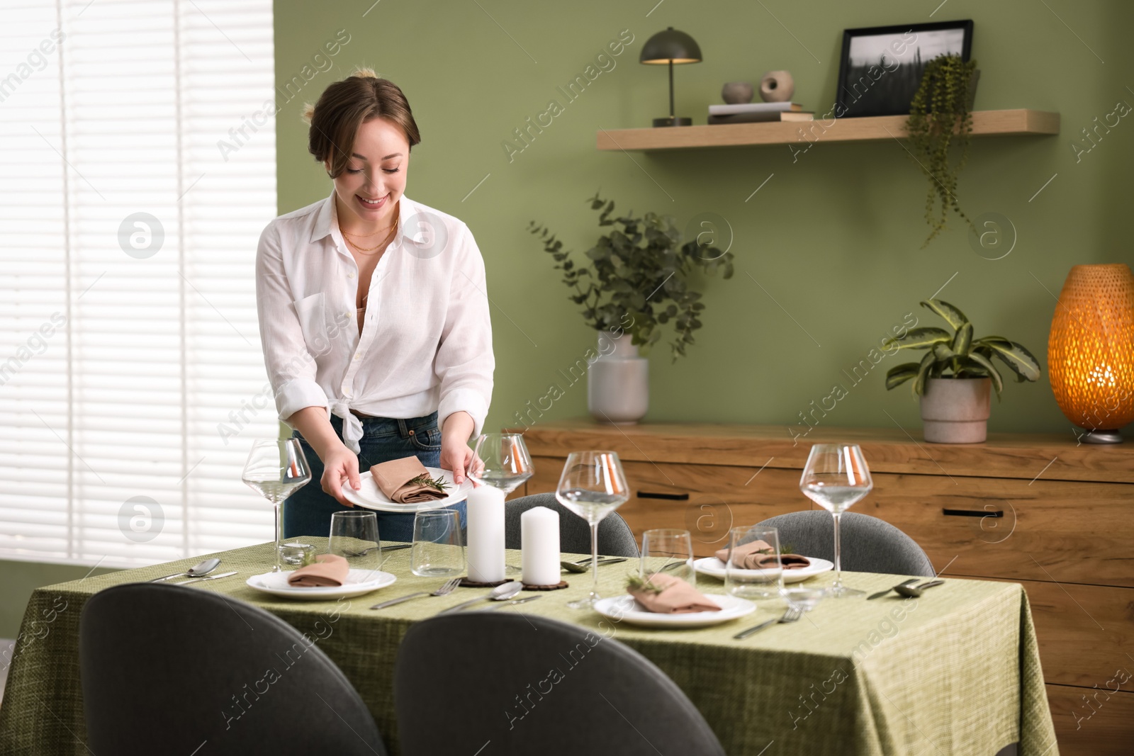 Photo of Happy young woman setting table for dinner at home