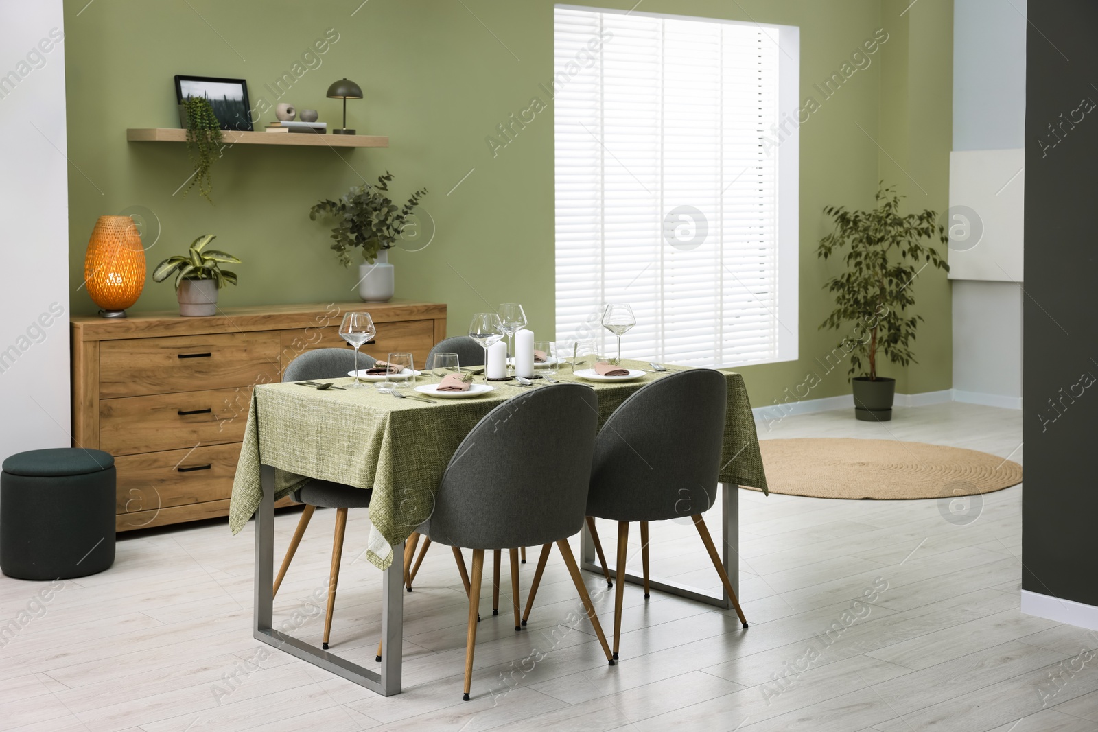 Photo of Stylish table setting with olive tablecloth, glasses and candles in dining room