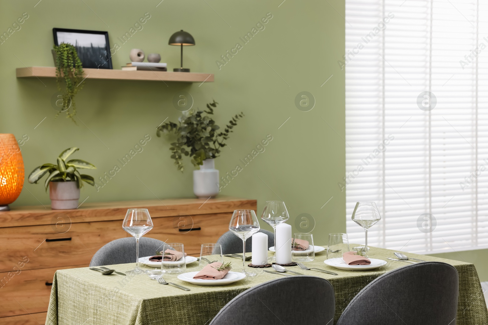 Photo of Stylish table setting with olive tablecloth, glasses and candles in dining room