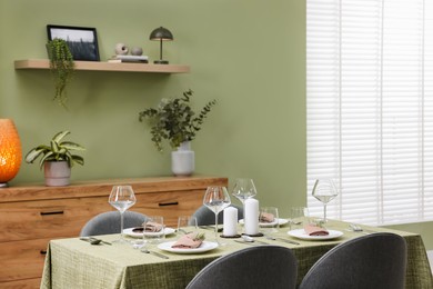 Photo of Stylish table setting with olive tablecloth, glasses and candles in dining room