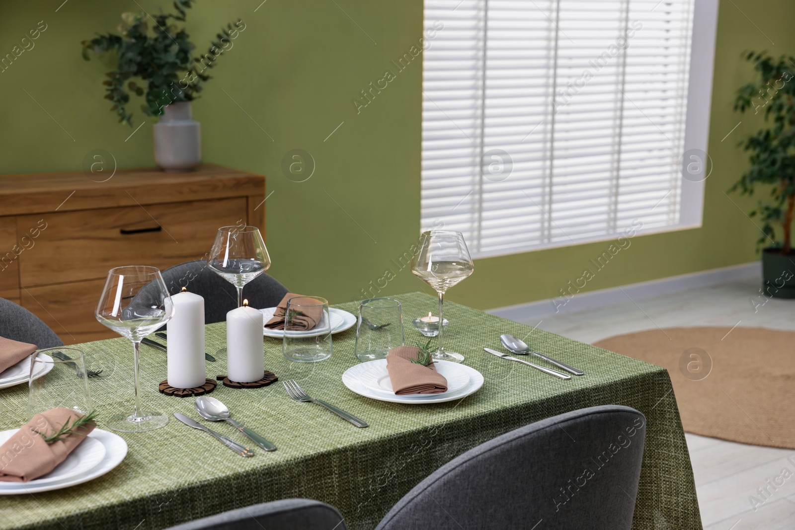 Photo of Stylish table setting with olive tablecloth, glasses and candles in dining room