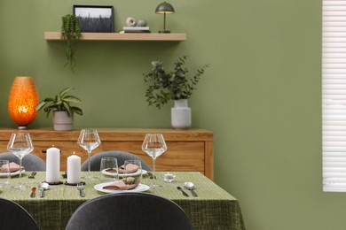 Photo of Stylish table setting with olive tablecloth, glasses and candles in dining room