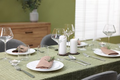 Stylish table setting with olive tablecloth, glasses and candles indoors