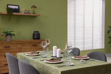 Photo of Stylish table setting with olive tablecloth, glasses and candles in dining room