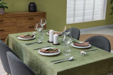 Stylish table setting with olive tablecloth, glasses and candles indoors