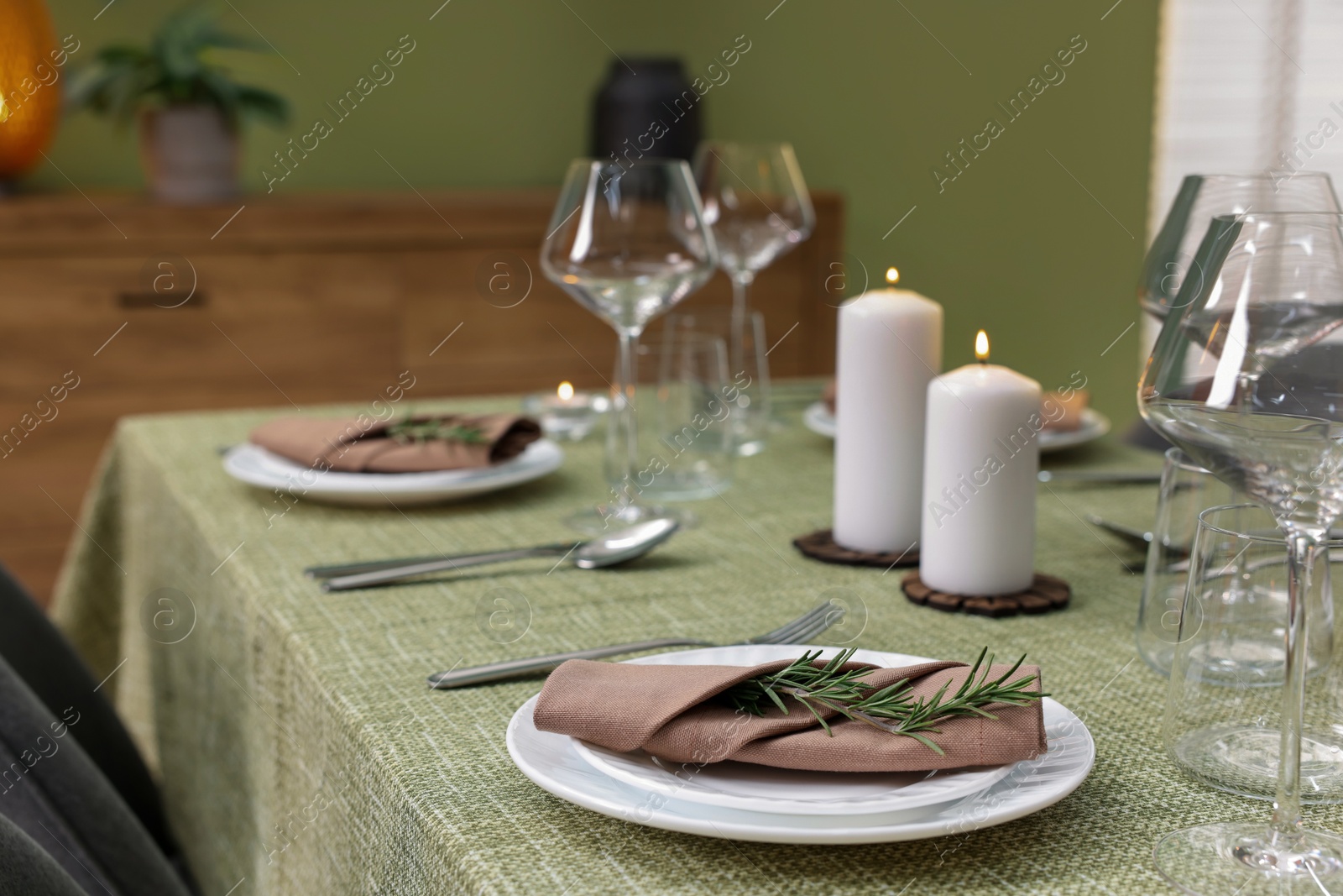 Photo of Stylish table setting with olive tablecloth, glasses and candles indoors