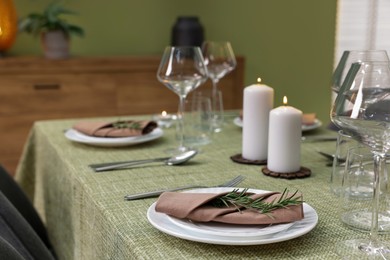 Stylish table setting with olive tablecloth, glasses and candles indoors