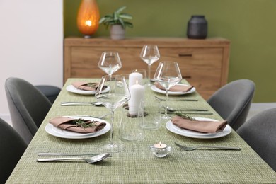 Stylish table setting with olive tablecloth, glasses and candles indoors