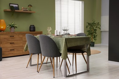 Photo of Stylish table setting with olive tablecloth, glasses and candles in dining room