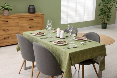 Photo of Stylish table setting with olive tablecloth, glasses and candles in dining room