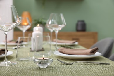 Photo of Stylish table setting with olive tablecloth, glasses and candles indoors, closeup