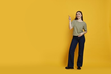 Photo of Smiling woman in stylish jeans pointing at something on orange background. Space for text