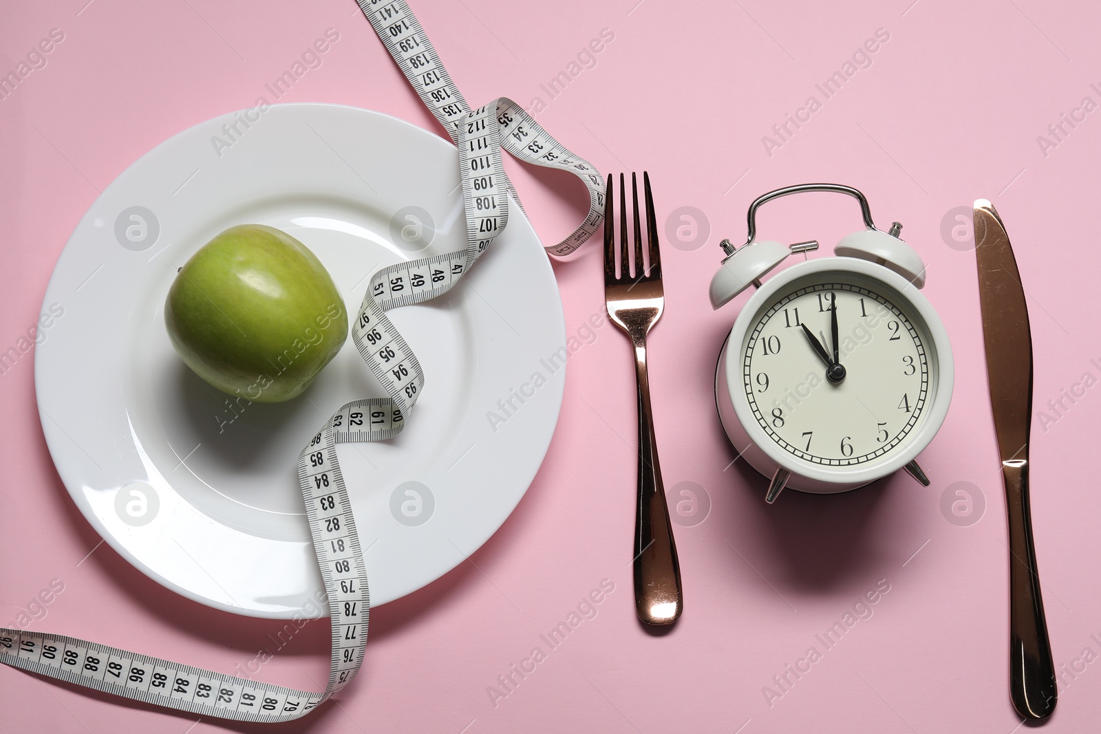 Photo of Alarm clock, plate, cutlery, apple and measuring tape on pink background, flat lay