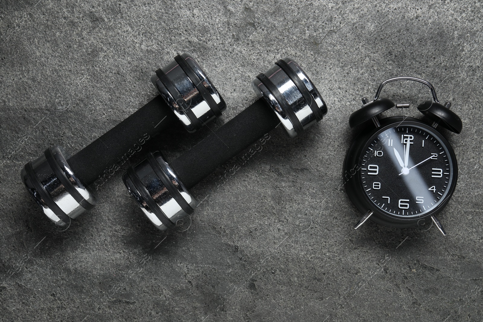 Photo of Alarm clock and dumbbells on grey background, flat lay