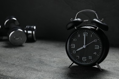 Photo of Alarm clock and dumbbells on grey background