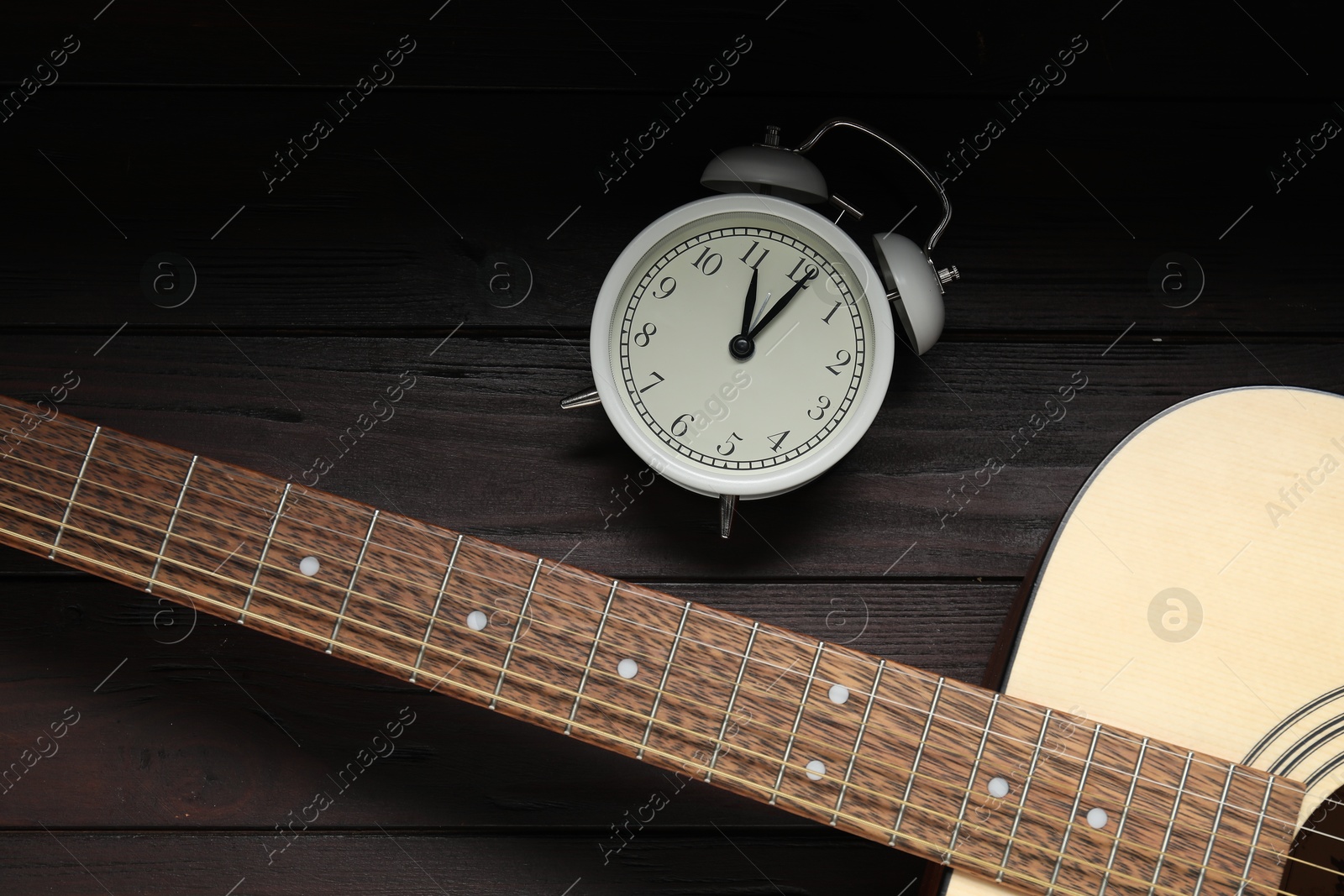 Photo of Alarm clock and guitar on wooden background, flat lay