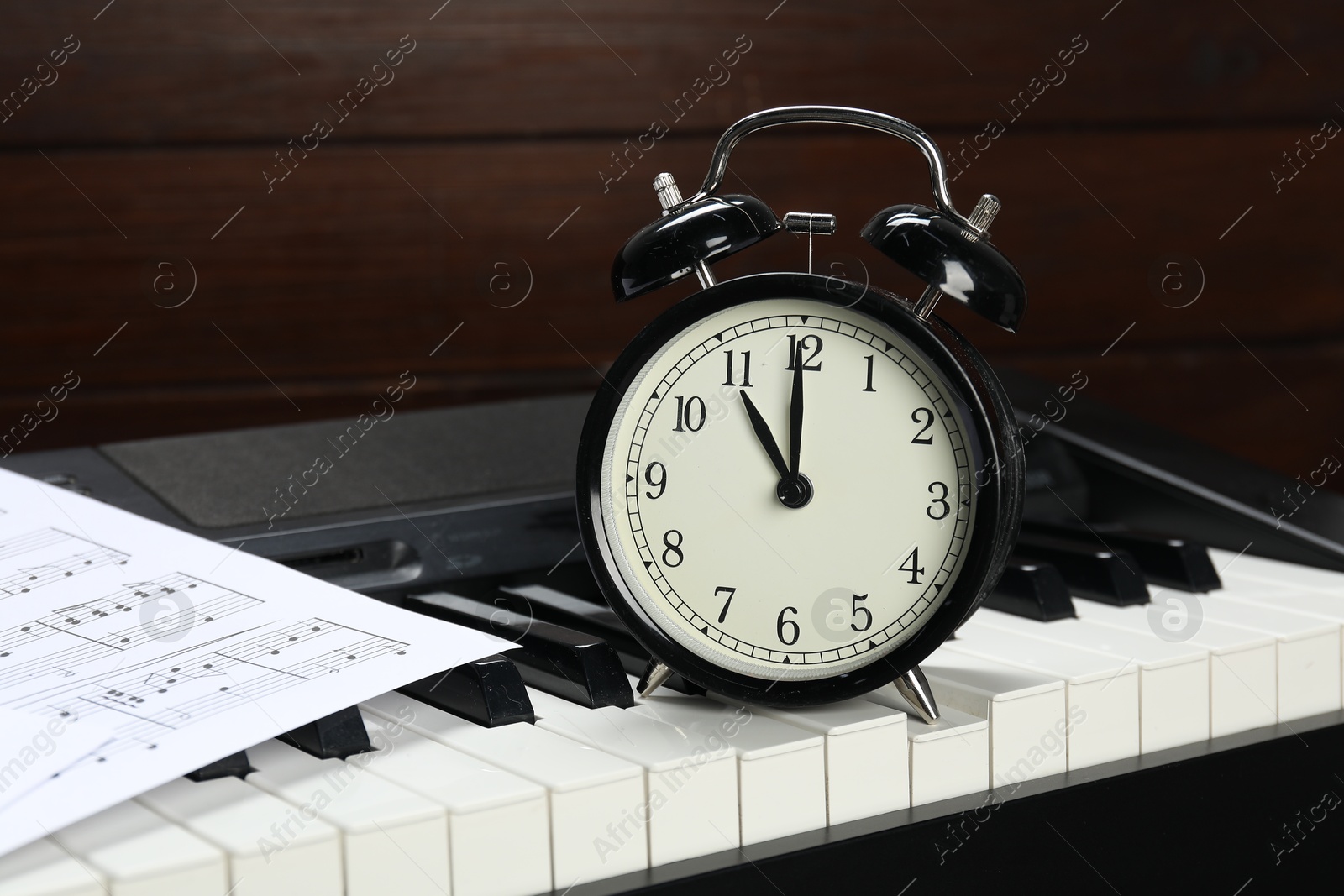 Photo of Alarm clock, note sheet and electric piano on wooden background