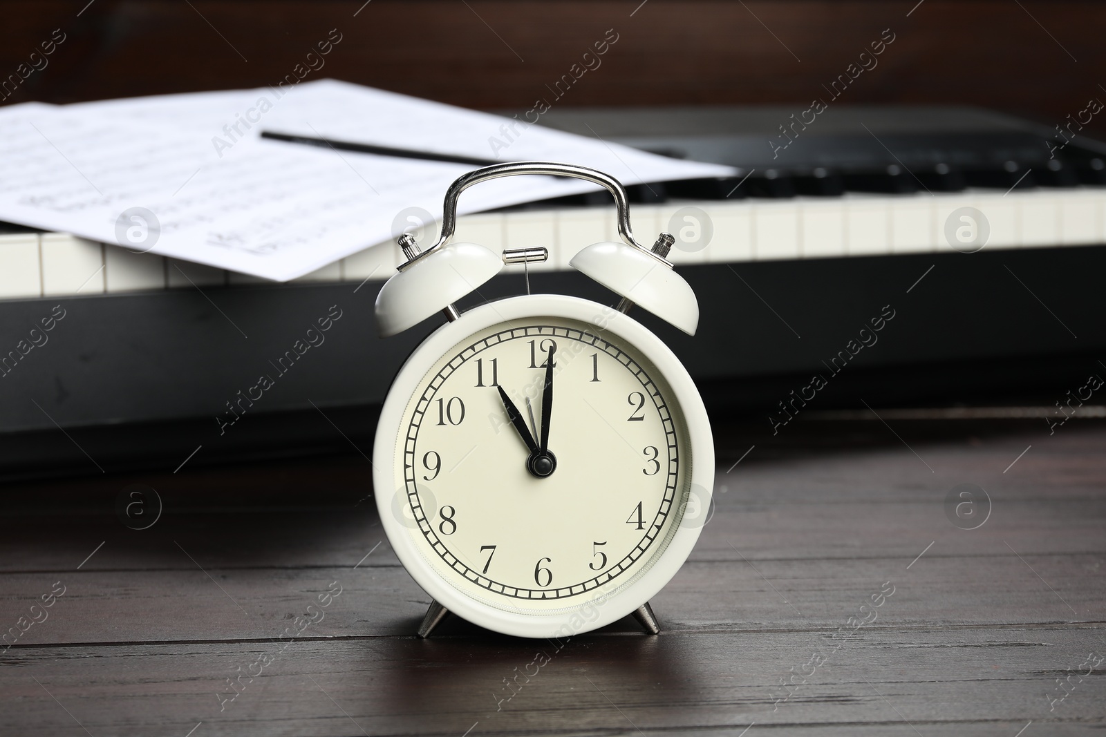 Photo of Alarm clock, note sheet and electric piano on wooden background