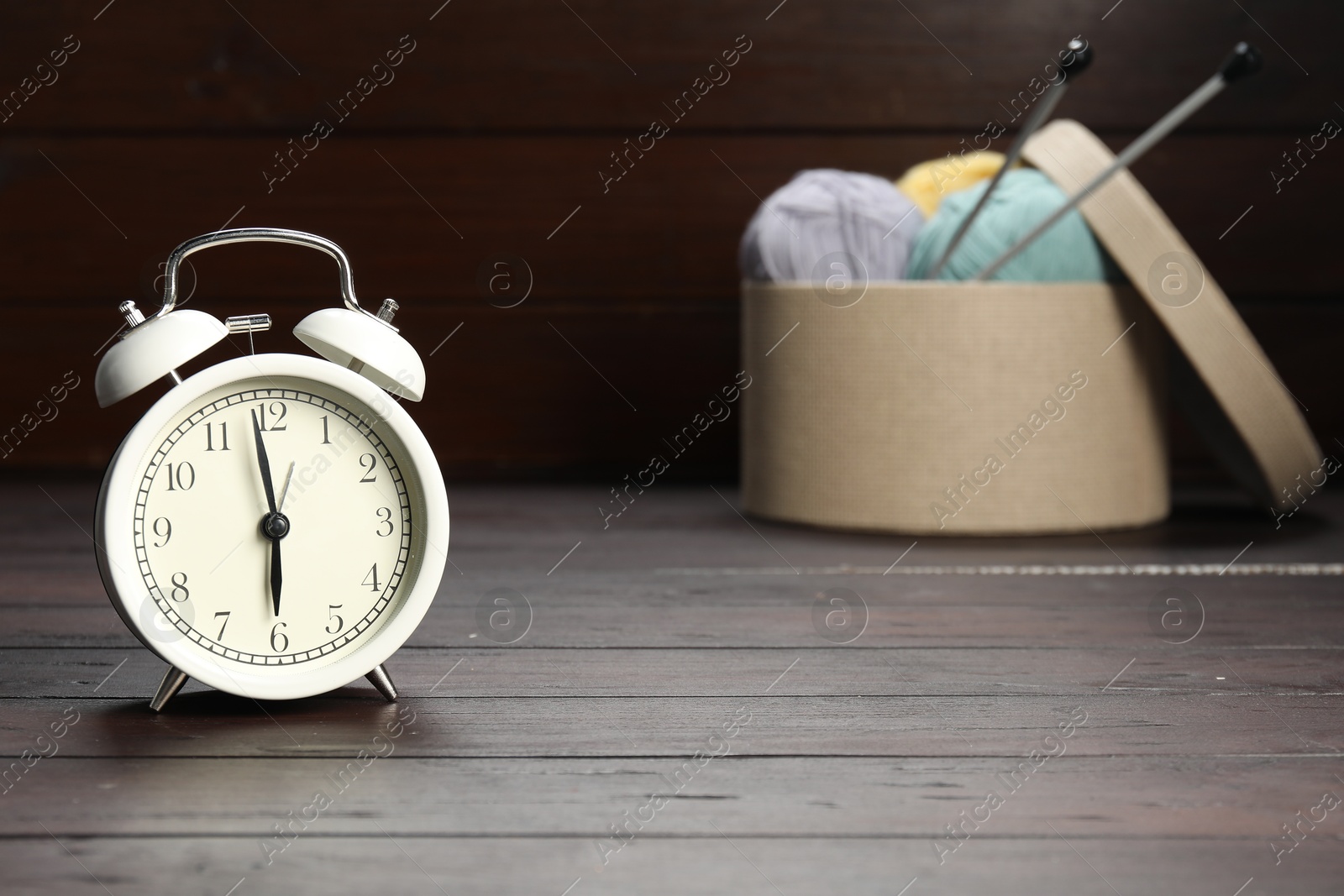 Photo of Alarm clock, yarn and knitting needles on wooden background