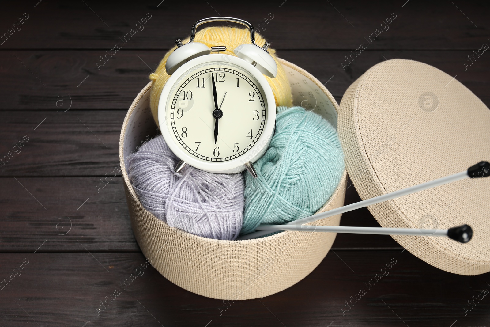 Photo of Alarm clock, yarn and knitting needles on wooden background