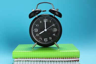 Photo of Alarm clock and notebooks on light blue background