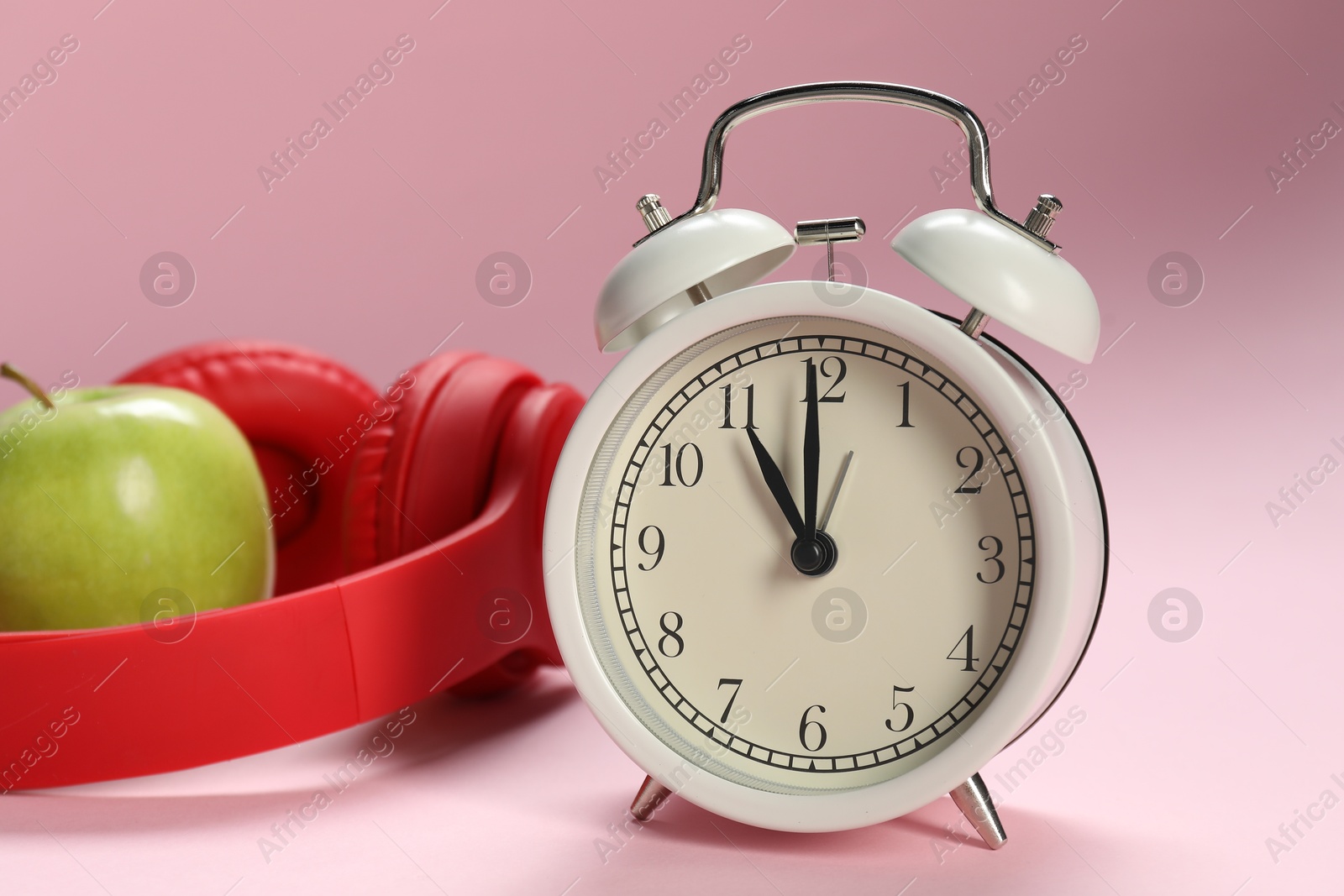 Photo of Alarm clock, headphones and apple on pink background