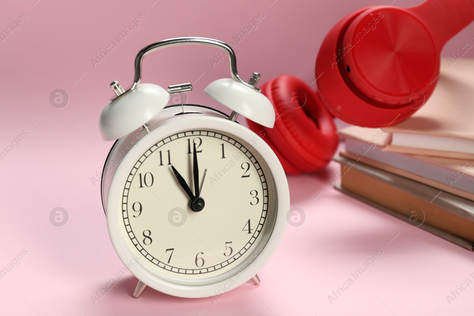 Photo of Alarm clock, books and headphones on light pink background