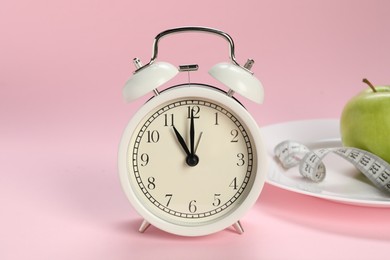 Photo of Alarm clock, plate, apple and measuring tape on pink background