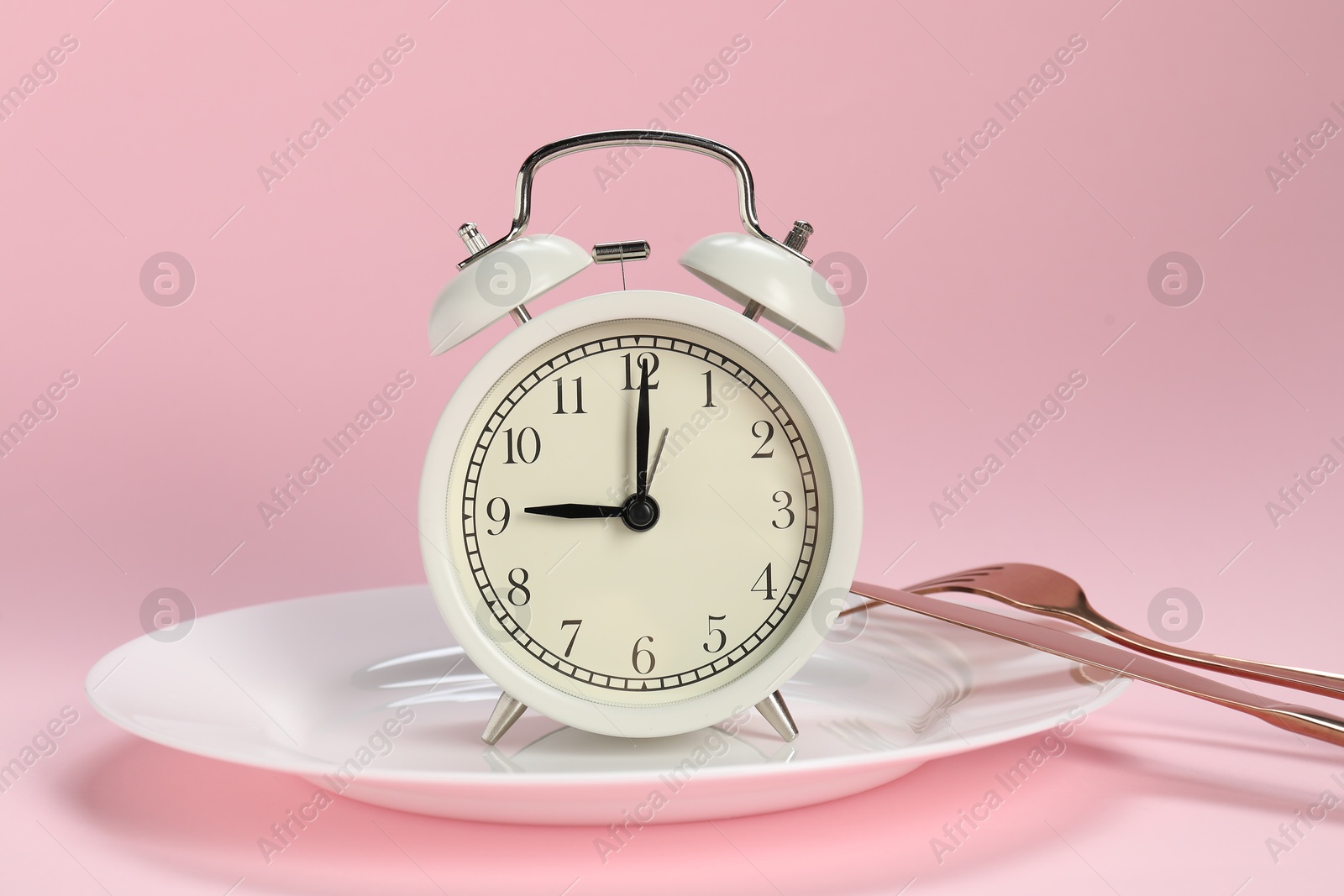 Photo of Alarm clock, plate and cutlery on pink background