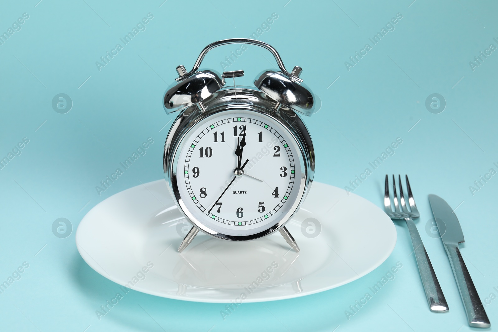 Photo of Alarm clock, plate and cutlery on light blue background