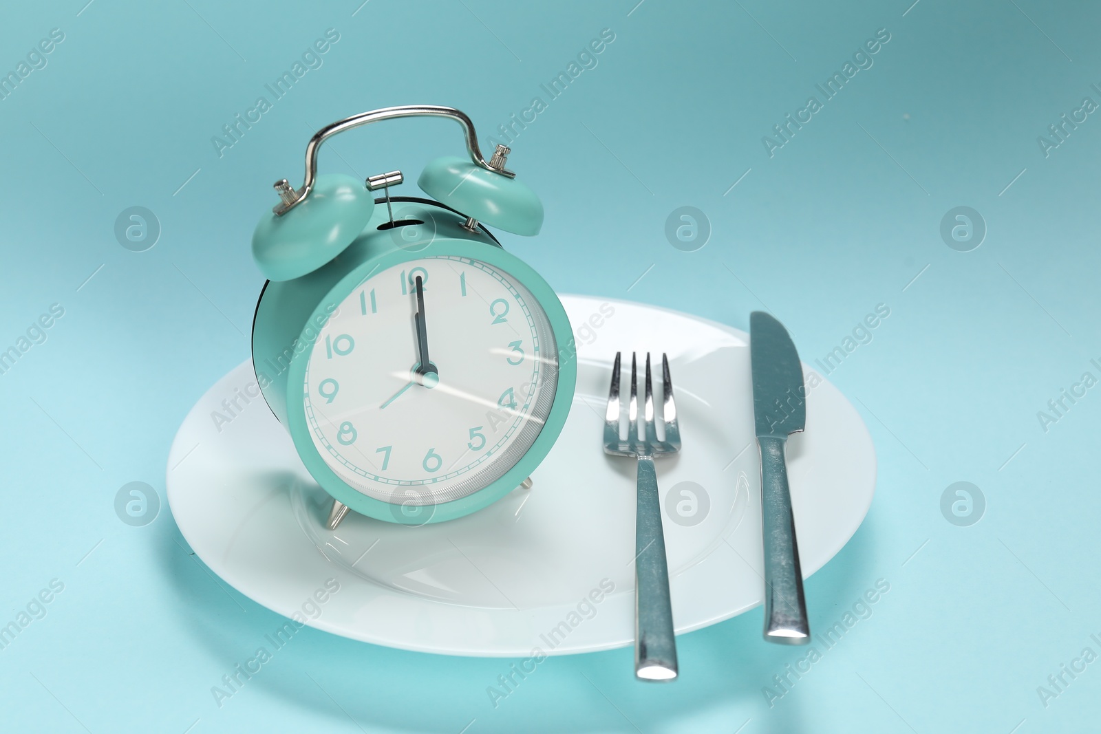 Photo of Alarm clock, plate and cutlery on light blue background